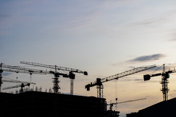 Construction cranes silhouetted against a cloudy sky