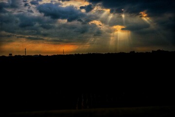 Sun rays stream through dense clouds over a dark silhouette of the horizon during sunset, creating a breathtaking dramatic atmosphere that highlights the beauty of nature.