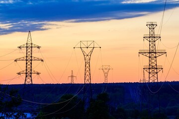 High-voltage transmission line masts against sunset sky.