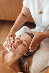 A woman receives a relaxing facial massage and skin care in a tranquil spa setting with soft warm...