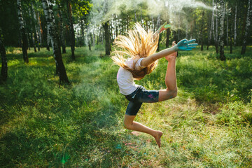 Caucasian girl jumps barefoot in powder cloud in sunny forest. Powerful artistic motion, freedom, youthful energy, expression, creativity and individuality in summer nature.