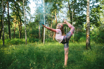 Smiling Caucasian girl in gymnastics pose with colored powder in forest. Concept of empowerment,...