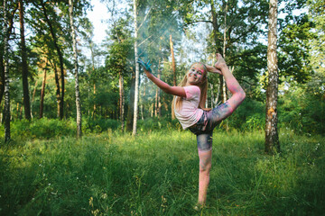 Smiling girl with colored powder confidently holds gymnastics pose in forest. Concept of...