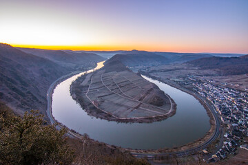 Sunrise over the Moselle. The river winds through a valley in a narrow loop surrounded by vineyards...