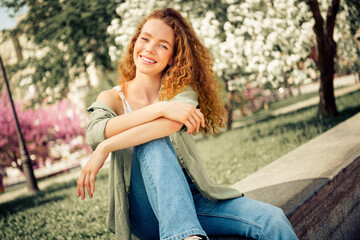 Obraz premium Young smiling woman enjoying a sunny day outdoors in a picturesque floral park with casual style and relaxed posture