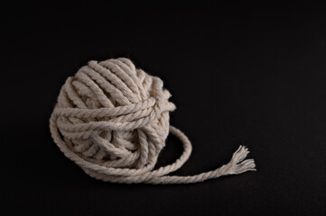 A neatly wound ball of natural twine sits against a dark background, highlighting its texture and...
