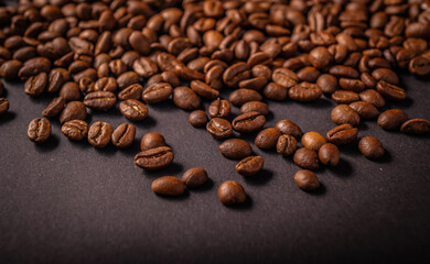 Freshly roasted coffee beans lie scattered across a dark background, highlighting their glossy...