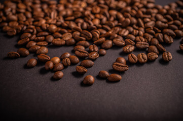 Coffee beans of various shapes and sizes are spread across a dark surface, showcasing their rich brown color and texture perfect for brewing