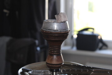 Close-up of a hookah bowl filled with flavored tobacco and topped with glowing hot charcoal. The coals emit a warm, reddish glow, creating a cozy and atmospheric scene.