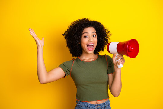 Cheerful young woman with curly hair holds a megaphone, spreading joy against a vibrant yellow background