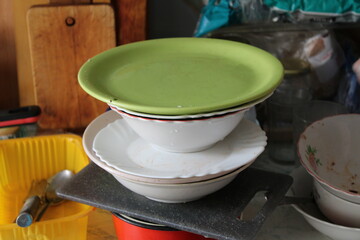 A tall stack of unwashed dirty dishes in a kitchen.Plates, bowls, and utensils are piled up with food residue, creating a messy and realistic domestic scene.
