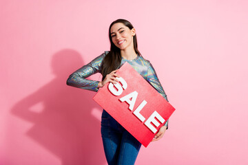 Young woman holding a sale sign against a vibrant pink background, showcasing a cheerful expression...