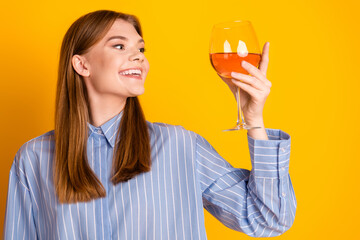 Young woman joyfully holding a glass of rose wine against a bright yellow background, expressing...
