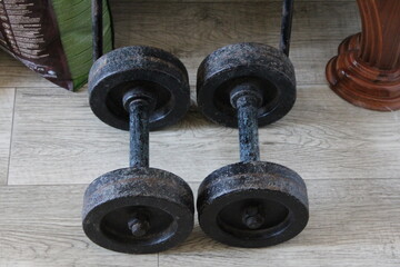 Rustic and nostalgic scene of two old cast iron dumbbells resting on a textured wooden floor.