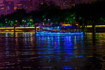 Fototapeta premium Colorful blue tourist boat, illuminated Hai River water reflection, Tianjin, China.