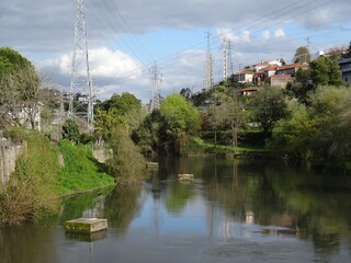 Fototapeta premium A river flows near a small village with electricity pylons and power lines in Northern Portugal 