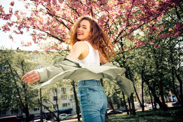 Young woman enjoying a sunny day in a blooming park, surrounded by vibrant spring blossoms, city...