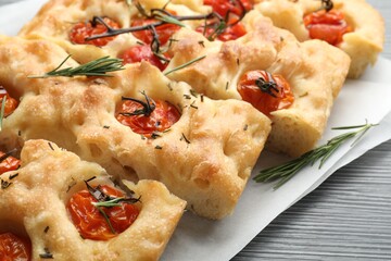 Cut delicious focaccia with tomatoes and spices on table, closeup