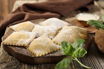Uncooked ravioli and basil on wooden table, closeup
