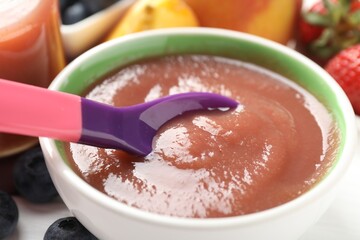 Baby food. Eating tasty puree with spoon at white table, closeup