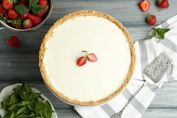 One tasty cheesecake, strawberries, mint and server on grey wooden table, flat lay