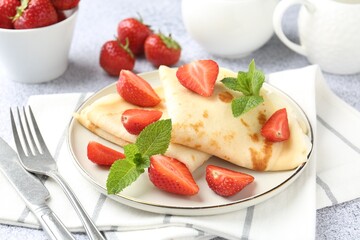 Tasty crepes with cream, strawberries and mint served on light gray table, closeup
