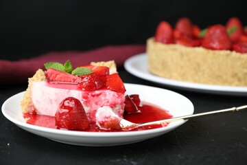 Piece of tasty cheesecake with strawberries, sauce and mint on black table, closeup