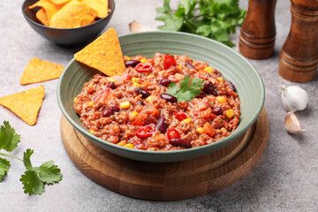 Tasty chili con carne in bowl and nachos on grey table, closeup