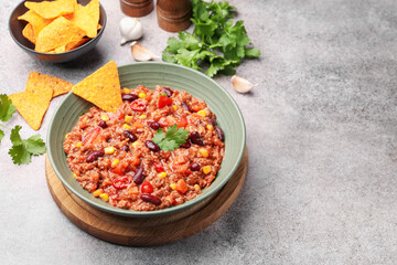 Tasty chili con carne in bowl and nachos on grey table, closeup. Space for text