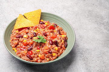 Tasty chili con carne in bowl and nachos on grey table, closeup. Space for text