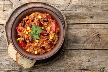 Tasty chili con carne in bowl and bread slices on wooden table, top view. Space for text