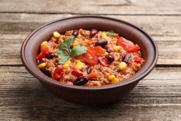 Tasty chili con carne in bowl on wooden table, closeup