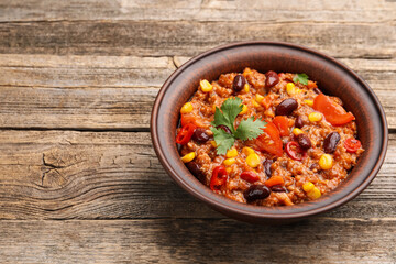 Tasty chili con carne in bowl on wooden table, closeup. Space for text