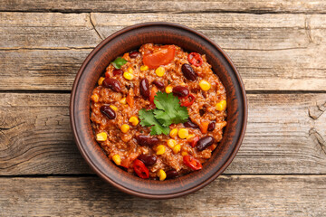 Tasty chili con carne in bowl on wooden table, top view