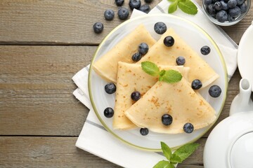 Tasty crepes with blueberries and mint on wooden table, flat lay. Space for text
