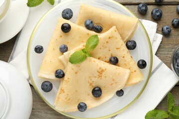 Tasty crepes with blueberries and mint on wooden table, flat lay