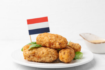 Tasty fried croquettes, basil, sauce and flag of Netherlands on white tiled table, closeup