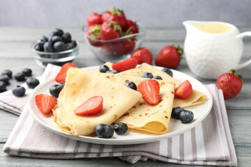 Delicious crepes with berries and cream on grey wooden table, closeup