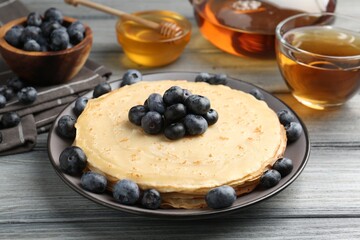 Delicious crepes with blueberries, honey and tea on grey wooden table, closeup