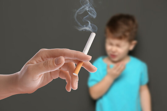 Passive smoking. Little boy coughing because of man smoking nearby on grey background. Selective focus
