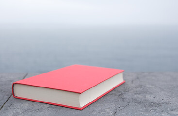 Red hardcover book on stone surface with ocean in background with copy space.