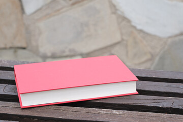 Red hardcover book lying on wooden bench with stone background with copy space.