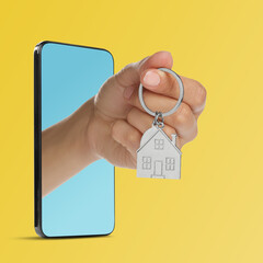 Woman's hand with keychain in shape of house sticking out from smartphone on yellow background....