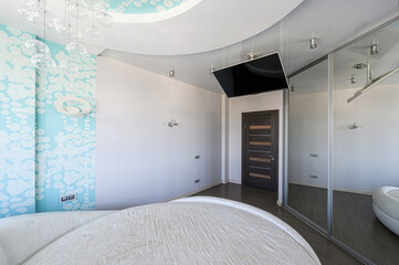 Bright bedroom with a round bed. The ceiling features a cloud design and a modern chandelier. A...