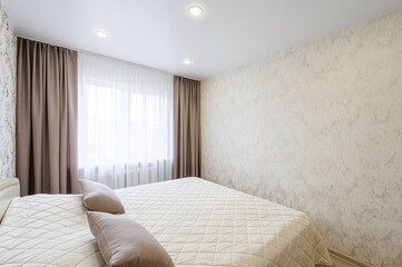 bright bedroom features floral wallpaper, a double bed with cushions, and curtains framing a...