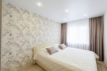 bright bedroom features floral wallpaper, a double bed with cushions, and curtains framing a...