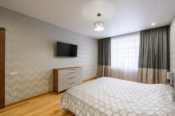 modern bedroom features a bed, dresser, and a wall-mounted TV. The room is decorated in neutral...