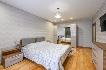 Cozy bedroom with wooden floors, chevron wallpaper, and a large bed with a patterned quilt. A...