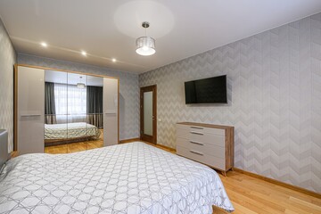 Cozy bedroom with wooden floors, chevron wallpaper, and a large bed with a patterned quilt. A mirrored wardrobe enhances the space. Natural light fills the room
