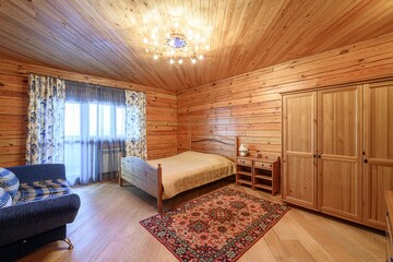 cozy wooden bedroom features a bed, wardrobe, sofa, & a rug. Wood paneling covers the walls &...